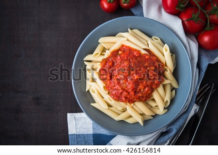 Penne pasta with tomato sauce on dark wooden background top view. Italian cuisine.