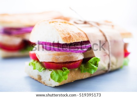 Healthy chicken sandwiches with lettuce salad, tomato and onion on blue wooden background close up.