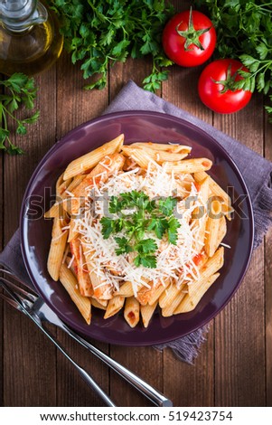 Penne pasta with chicken, tomato sauce, parmesan cheese and parsley on dark wooden background top view. Italian food.