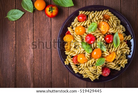 Fusilli pasta salad with pesto genovese, colorful tomatoes and basil leaves on dark wooden background top view. Italian food. Delicious meal. Space for text.