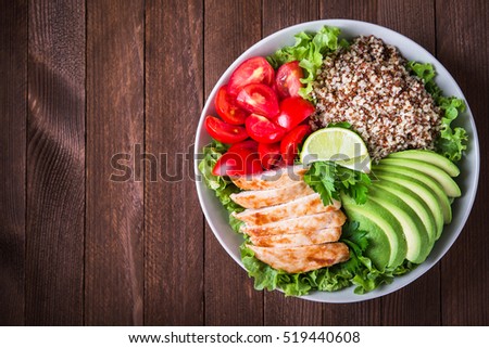 Healthy salad bowl with quinoa, tomatoes, chicken, avocado, lime and mixed greens, lettuce, parsley on wooden background top view. Food and health. Space for text.