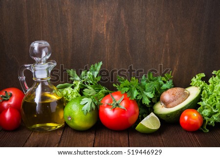 Fresh tomatoes, lime, avocado, lettuce, parsley and olive oil on dark wood background with space for text. Healthy food. Vegetables and greens. Salad ingredients.