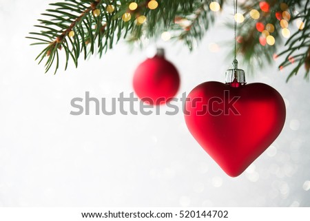 Red christmas ornaments, heart and ball, on the xmas tree on glitter bokeh background with twinkle lights. Merry christmas card. Winter holiday theme. Happy New Year. Space for text.