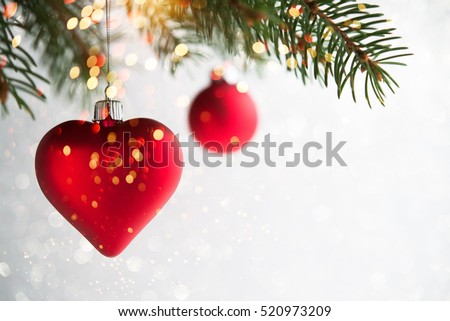 Red christmas ornaments, heart and ball, on the xmas tree on glitter bokeh background with twinkle lights. Merry christmas card. Winter holiday theme. Happy New Year. Space for text.