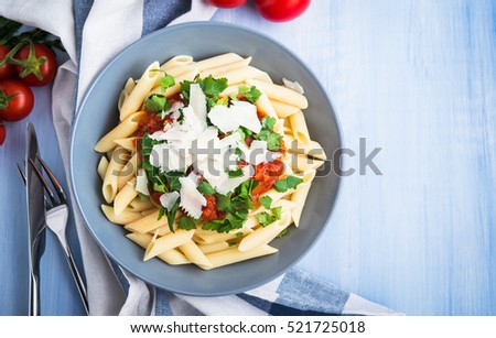 Penne pasta with tomato sauce, parsley and parmesan cheese on blue wooden background top view. Italian food. Delicious meal.