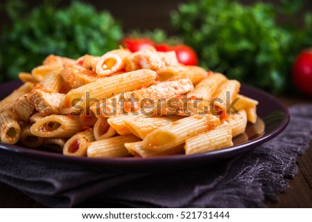 Penne pasta with chicken and tomato sauce on dark wooden background close up. Italian food. Delicious meal.