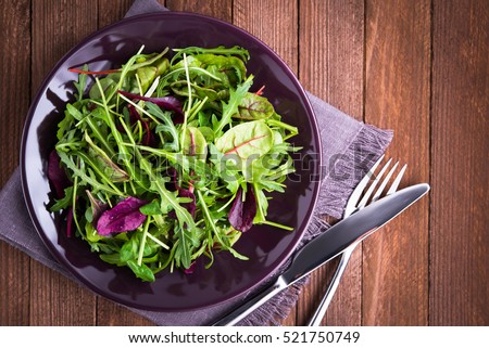 Fresh salad plate with mixed greens (arugula, mesclun, mache) on dark wooden background top view. Healthy food. Green meal.
