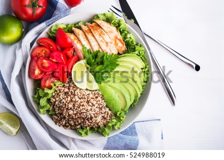 Healthy salad bowl with quinoa, tomatoes, chicken, avocado, lime and mixed greens, lettuce, parsley, on white wood background top view. Food and health. Superfoods meal.