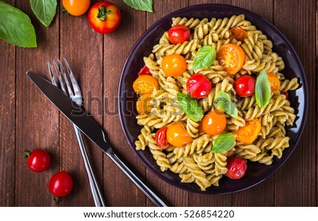 Fusilli pasta salad with pesto genovese, colorful tomatoes and basil leaves on dark wooden background top view. Italian food. Delicious meal.