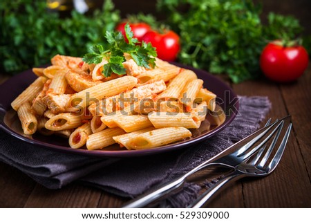 Penne pasta dish with chicken and tomato sauce on dark wooden background close up. Italian food. Delicious meal.