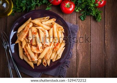 Penne pasta dish with chicken and tomato sauce on dark wooden background top view. Italian food. Delicious meal.