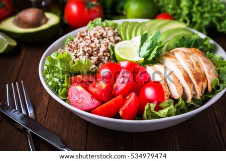 Healthy salad plate with quinoa, cherry tomatoes, chicken, avocado, lime and mixed greens, lettuce, parsley on wooden background close up. Food and health. Superfood meal