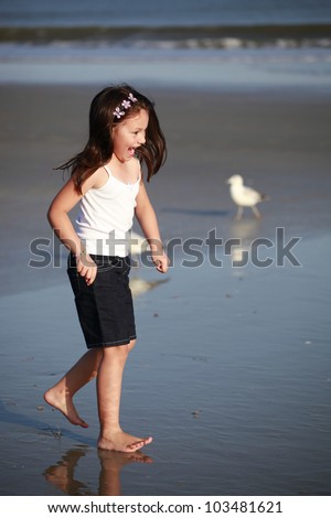 cute young girl, barefoot on the wet beach sand in jean shorts and a t-shirt late in the afternoon