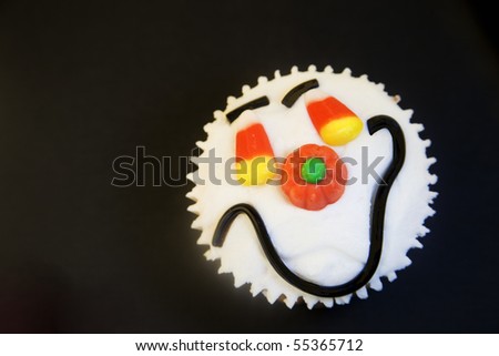 Halloween happy face cupcake decorated with candy corn, pumpkin and licorice smile on black background.