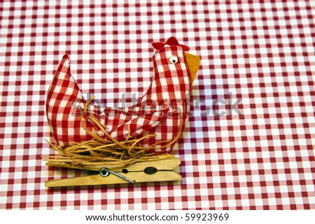 Stuffed fabric hen on a nest made out of red and white gingham fabric over a gingham background