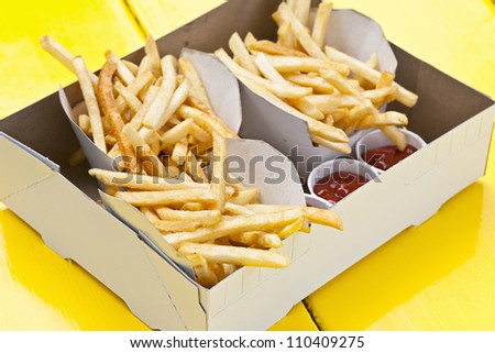 Portions of french fried potatoes with ketchup in cardboard take-out box