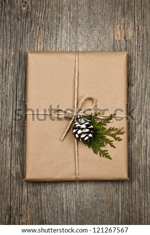 Christmas gift in brown wrapping and string with pine cone decoration on old wood background