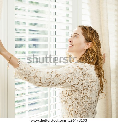 Happy woman looking out big bright window with curtains and blinds
