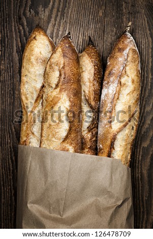 Four Baguette Bread Loaves In Paper Bag On Wooden Background