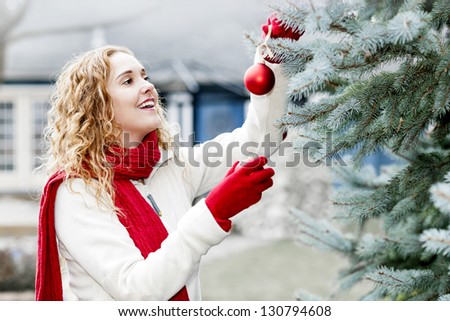 Portrait of smiling woman hanging Christmas ornaments on spruce tree outdoors in yard near home