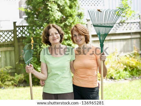 Mother and daughter holding rakes gardening doing yard work outside