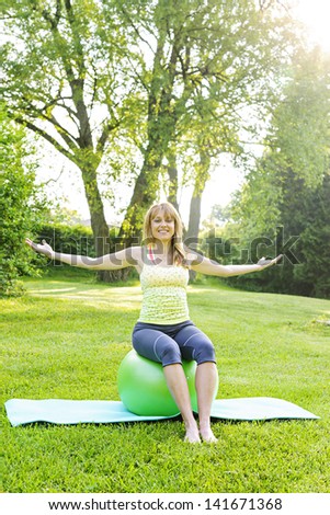Female fitness instructor sitting on yoga exercise ball in green park