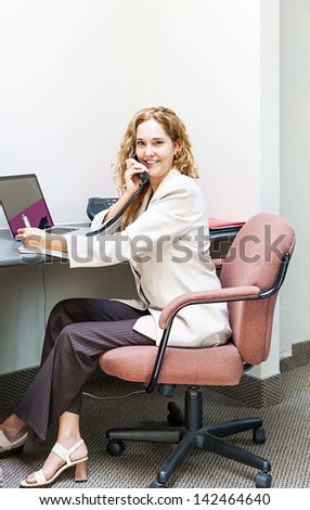 Businesswoman on phone talking and taking notes in office workstation