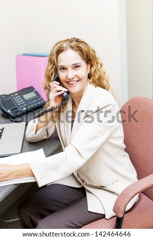 Smiling businesswoman on phone in office workstation