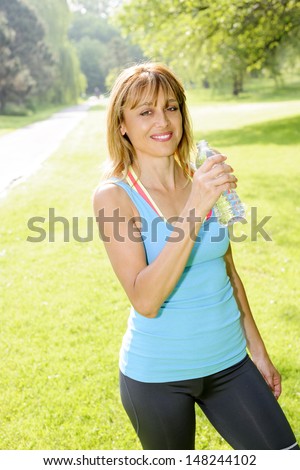 Smiling female fitness instructor taking a break with water bottle while exercising outdoor
