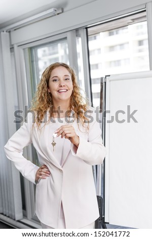 Smiling female real estate agent offering keys standing with blank flip chart