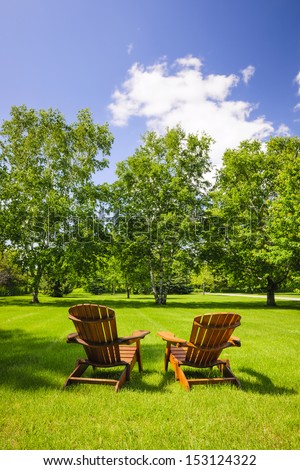 Two wooden adirondack chairs on lush green lawn with trees