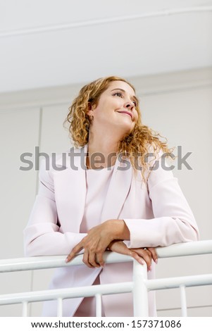Profile of confident successful business woman standing in office hallway leaning on railing shot from below