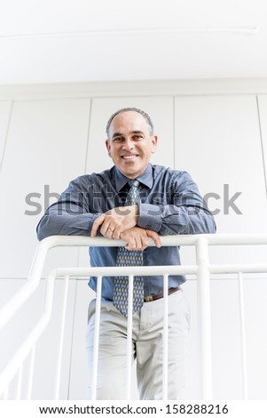 Smiling proud business man standing in office hallway leaning on railing