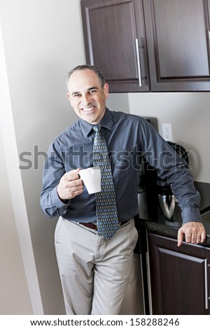 Smiling businessman standing holding coffee cup in office kitchen