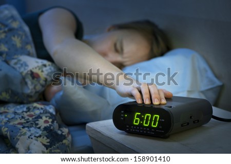 Young Woman Pressing Snooze Button On Early Morning Digital Alarm Clock Radio