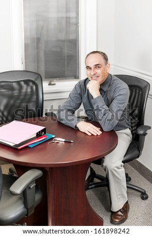 Middle aged business man looking happy sitting at table in office meeting room