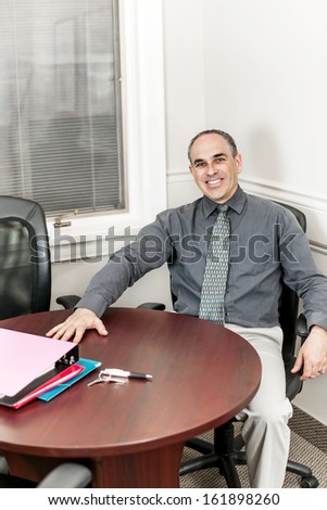Smiling middle aged business man sitting at table in office meeting room