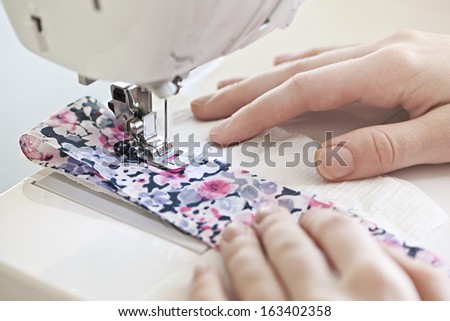 Closeup of hands guiding fabric through sewing machine needle and thread