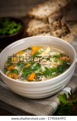 Chicken rice soup with vegetables in bowl and bread on rustic table
