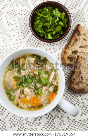 Cup of hot chicken rice soup served with bread and parsley from above on crochet tablecloth