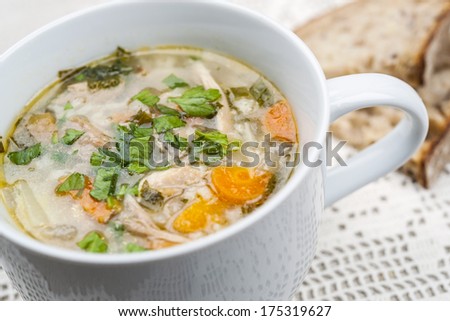 Cup of hot chicken rice soup served with bread on crochet tablecloth closeup