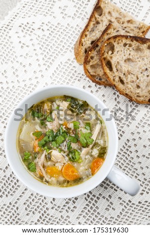 Cup of hot chicken rice soup served with bread from above on crochet tablecloth