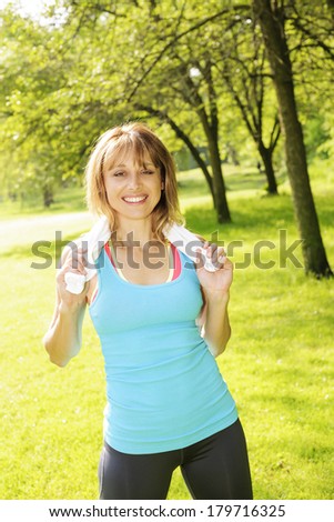 Female fitness instructor standing with towel around neck after exercising in green park