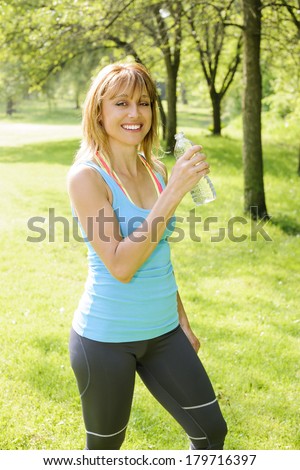 Smiling female fitness instructor taking a break  with water bottle while exercising outdoor