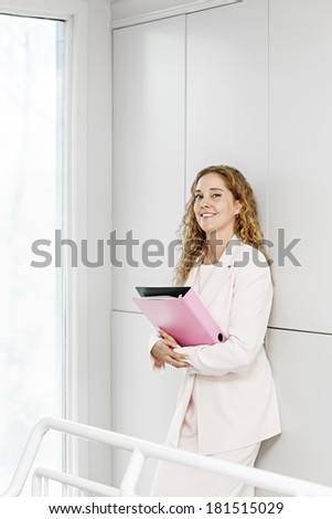 Confident career business woman standing in office hallway holding binder