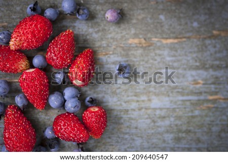 Fresh small wild strawberries and blueberries on old blue wooden background with copy space