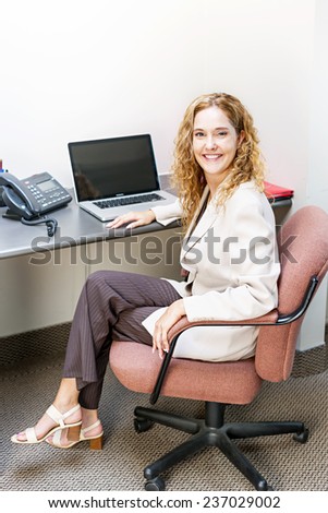 Happy businesswoman sitting at workstation in office with computer