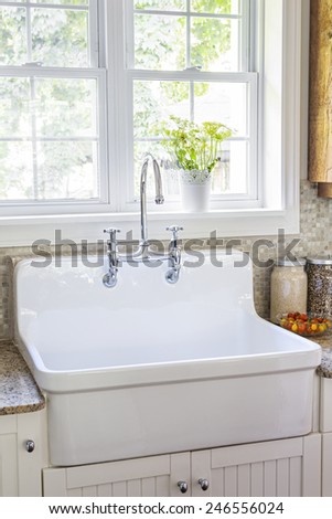 Kitchen interior with rustic white porcelain sink and granite stone countertop under large sunny window