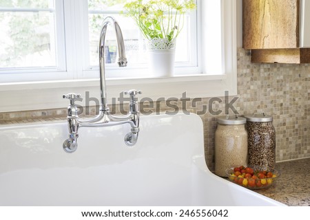 Rustic white porcelain kitchen sink with curved faucet and tile backsplash under large window