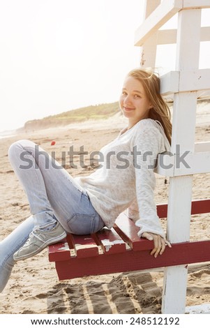 Young smiling woman sitting on lifeguard chair at Atlantic beach in Prince Edward Island, Canada.